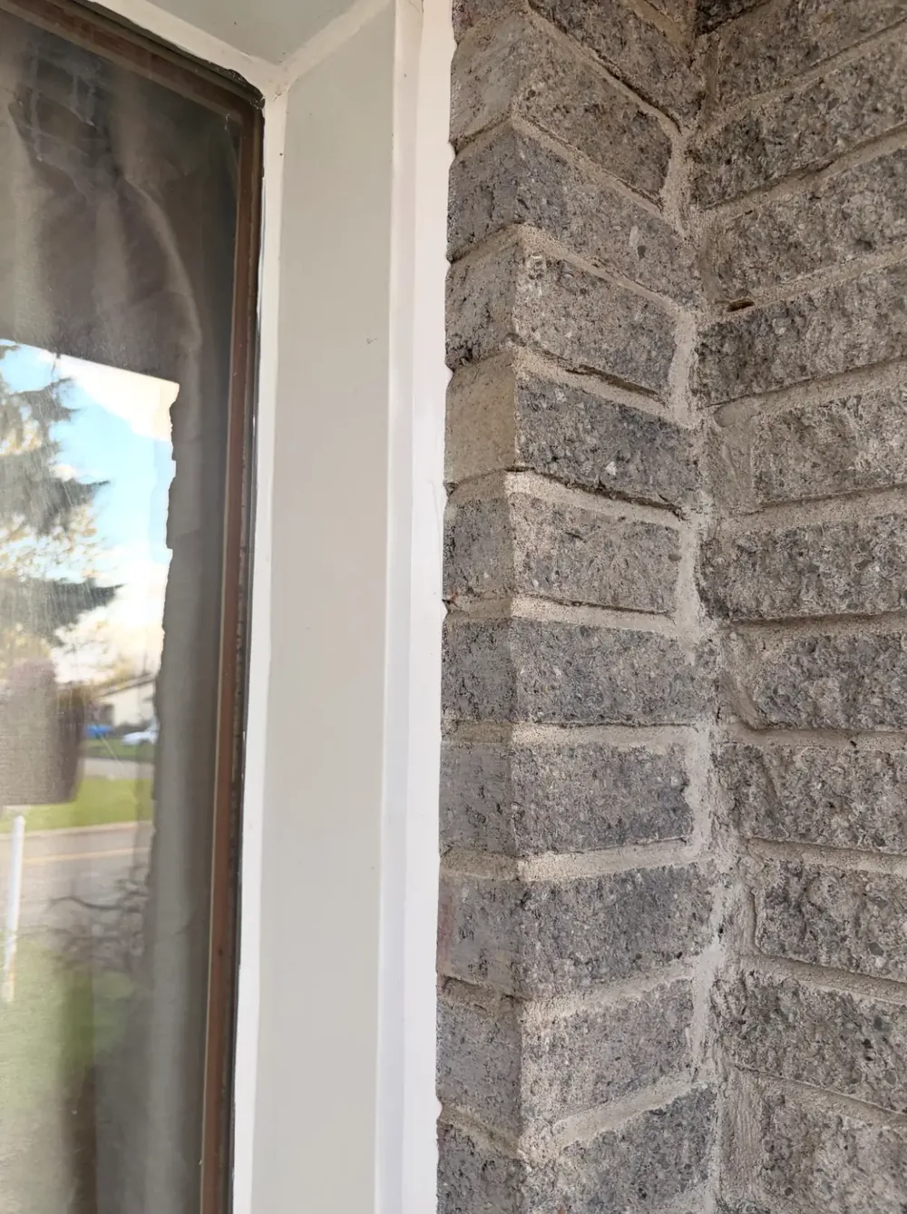 Joint vertical de scellant blanc entre le contour d'une fenêtre et un mur de brique / Vertical white sealant joint between a window casing and a brick wall